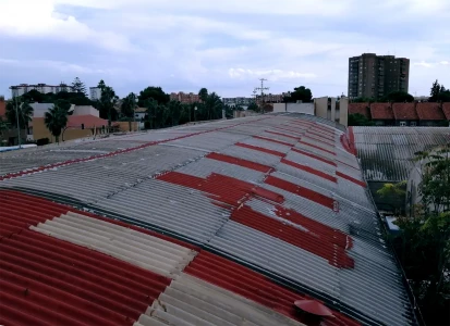 Antes de la aplicación de corcho proyectado Elasticover Tech. Preparativos previos a la aplicación de corcho proyectado rojo, Elasticover Tech, a una cubierta curva de una nave. con otras naves y chalets alrededor.