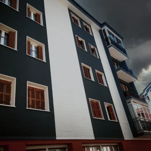 Aplicación de corcho proyectado ELASTICOVER TECH, en un edificio de viviendas. Fachada de un edificio, con cuatro plantas de viviendas, con corcho proyectado ELASTICOVER TECH, en franjas verticales blancas y azules oscuras.