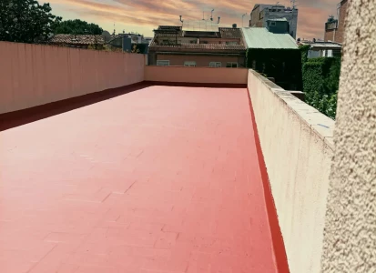Impermeabilización de terraza con fibra MAT Y ELASTICOVER IMPER. Terraza con la impermeabilización terminada, en color rojo, con vistas de casas alrededor.