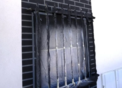 Aplicación de ELASTICOVER FINE y ELASTICOVER TECH imitación a ladrillo. Vista en detalle de una ventana con rejas, de una casa unifamiliar, protegida con plástico mientras se aplica ELASTICOVER FINE y ELASTICOVER TECH imitando ladrillos y bloques.