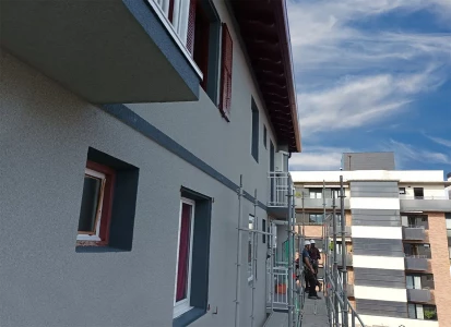 Aplicación de ELASTICOVER TECH. Detalle de la fachada de un edificio de cuatro plantas con andamios de obra.